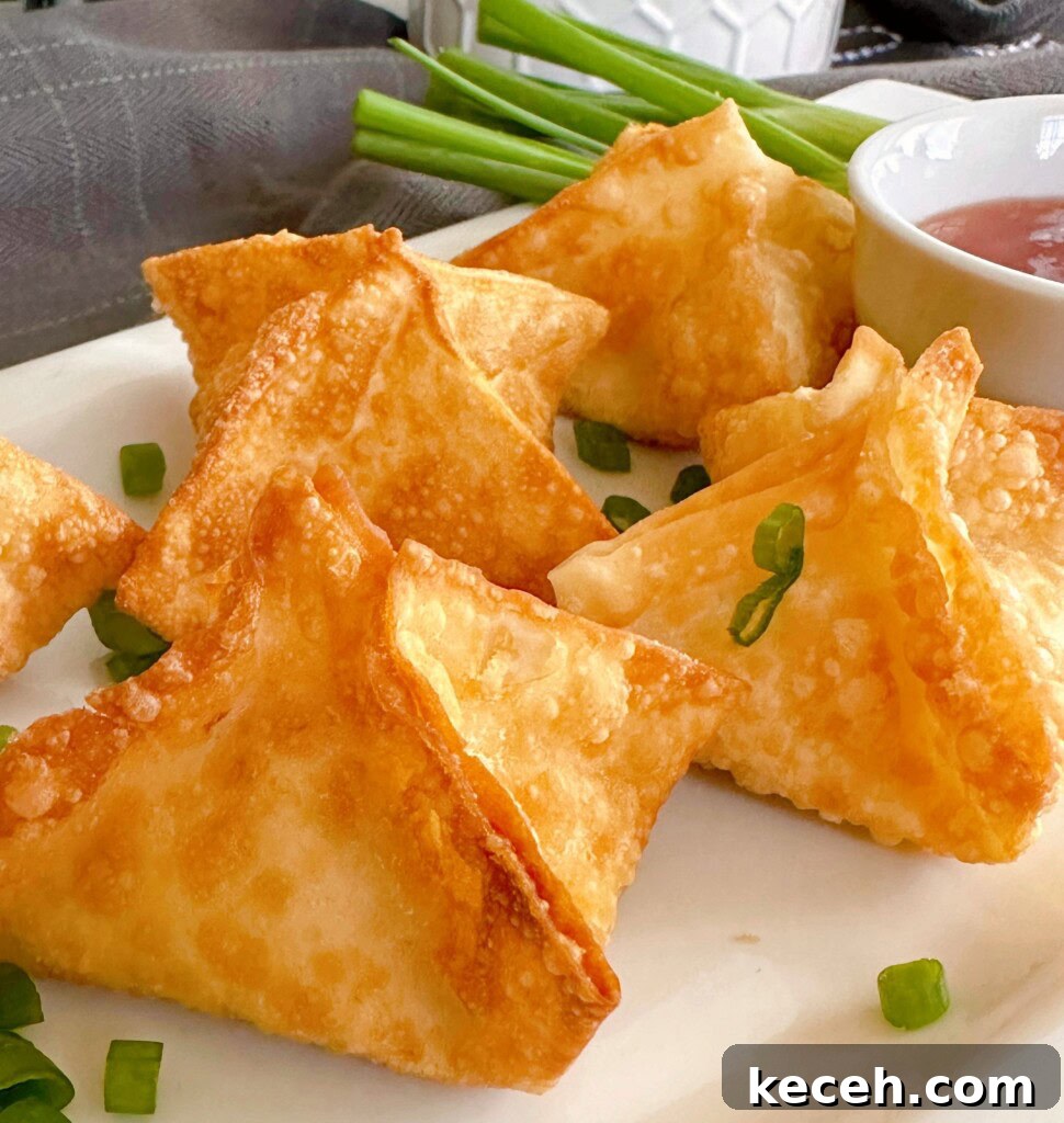 Classic Crab Rangoon Recipe: Crispy Crab & Cream Cheese Wontons 2 Cream cheese crab rangoons on a white serving platter with chopped green onions.