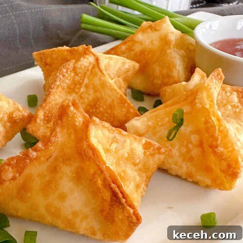 Classic Crab Rangoon Recipe: Crispy Crab & Cream Cheese Wontons 12 Cream cheese crab rangoons on a white serving platter with chopped green onions.