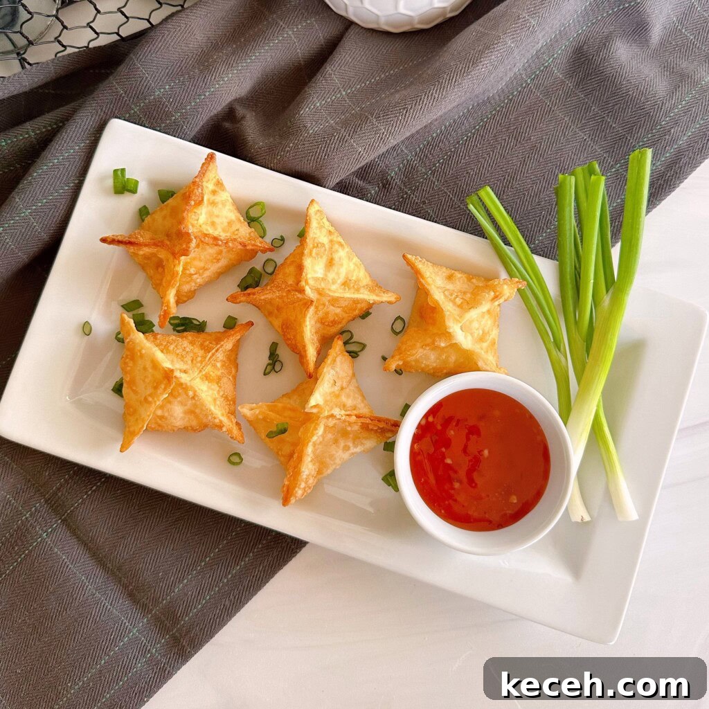 Classic Crab Rangoon Recipe: Crispy Crab & Cream Cheese Wontons 8 Fried wontons on a serving plate with sweet-and-sour sauce and green onions.