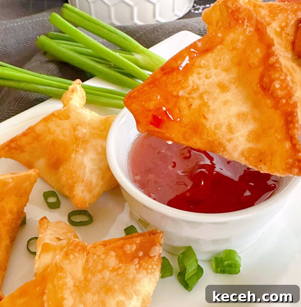 Classic Crab Rangoon Recipe: Crispy Crab & Cream Cheese Wontons 9 Crispy fried rangoon being dipped in sweet-and-sour sauce.