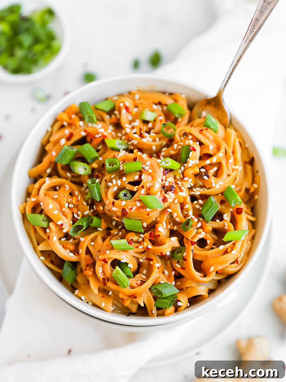 Spicy Peanut Noodle Recipe: Creamy Chili Sesame Noodles 2 A large bowl filled with creamy peanut noodles, garnished with sesame seeds and sliced green onions.