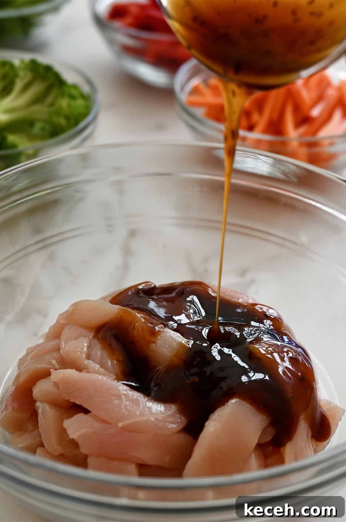 Sheet Pan Teriyaki Chicken with Roasted Vegetables 5 Pouring teriyaki sauce over strips of chicken breasts in a bowl.