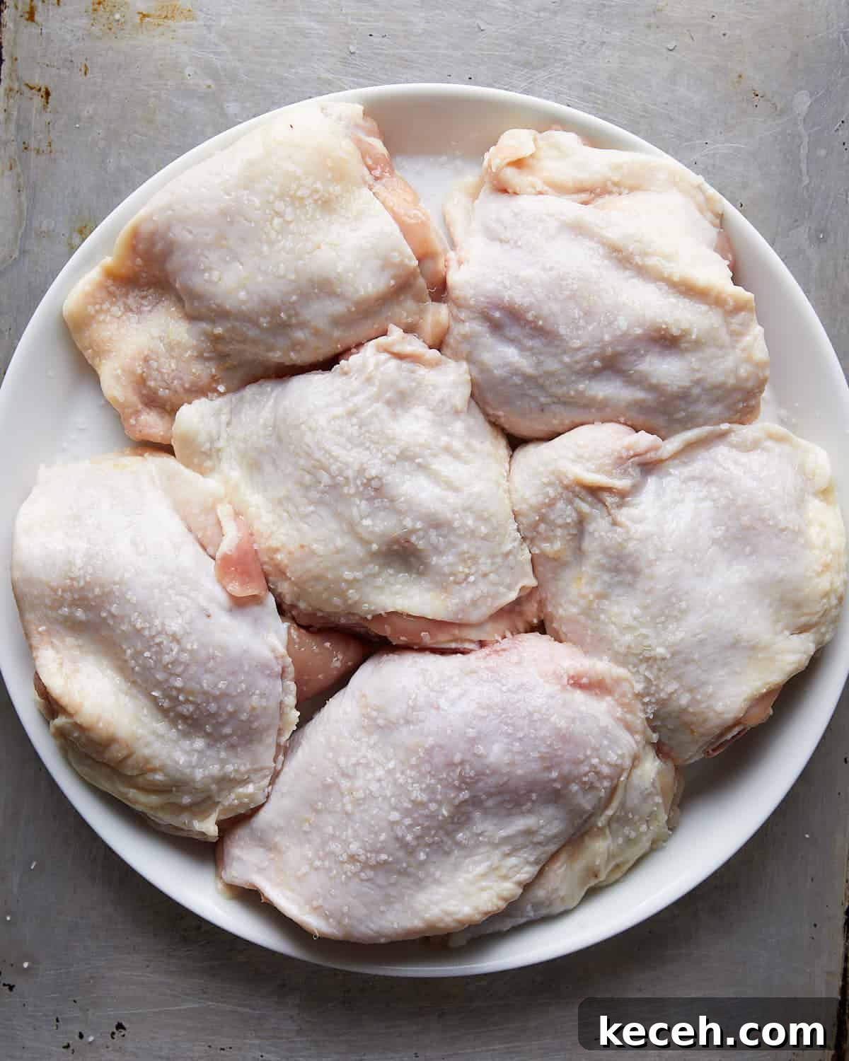 Crispy Baked Garlic Butter Chicken Thighs 4 Overhead shot of dry brine chicken thighs seasoned with kosher salt on white dish.
