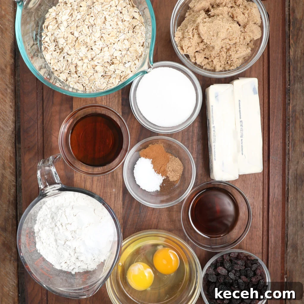 A top-down view of various baking ingredients in bowls on a wooden surface, perfect for making oatmeal raisin cookies—featuring oats, brown sugar, white sugar, flour, eggs, butter sticks, cinnamon, salt, vanilla, raisins, and a dark liquid.