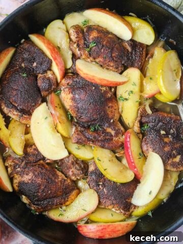 Apple cider chicken in a cast-iron skillet with a silver spoon.
