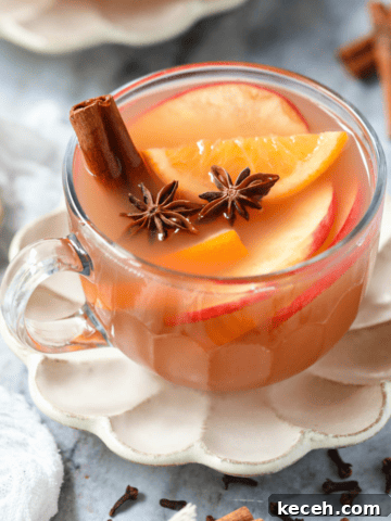 Homemade hot apple cider in a clear glass mug sitting on a gray marble surface.