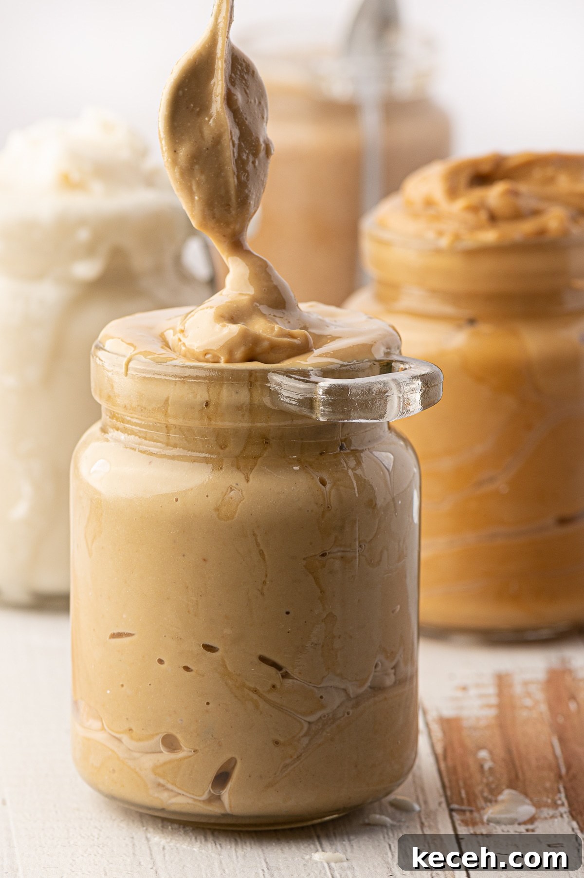 Jars of nut butters (peanut, cashew, coconut) on a rustic wooden background. 