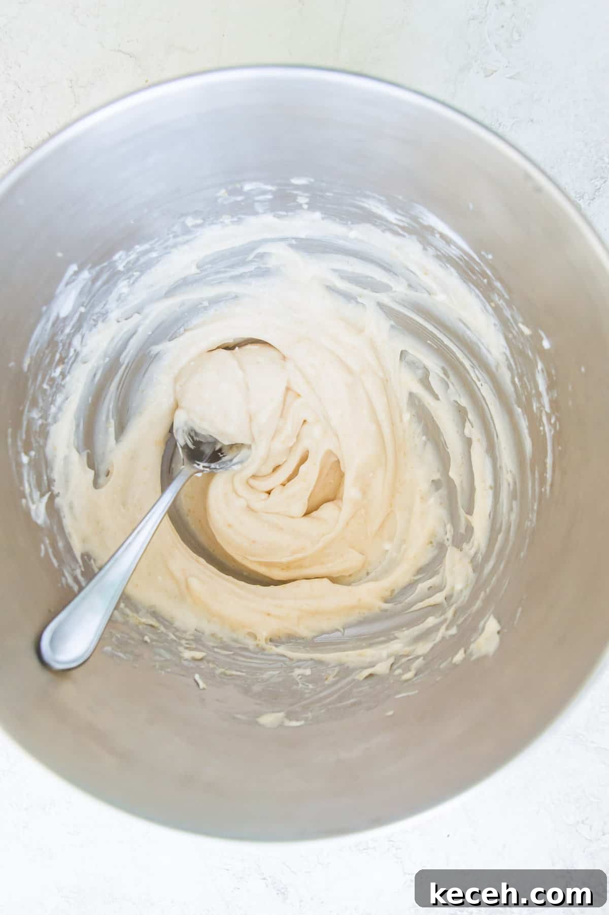 A bowl with cream cheese in it with a spoon in the cream cheese.