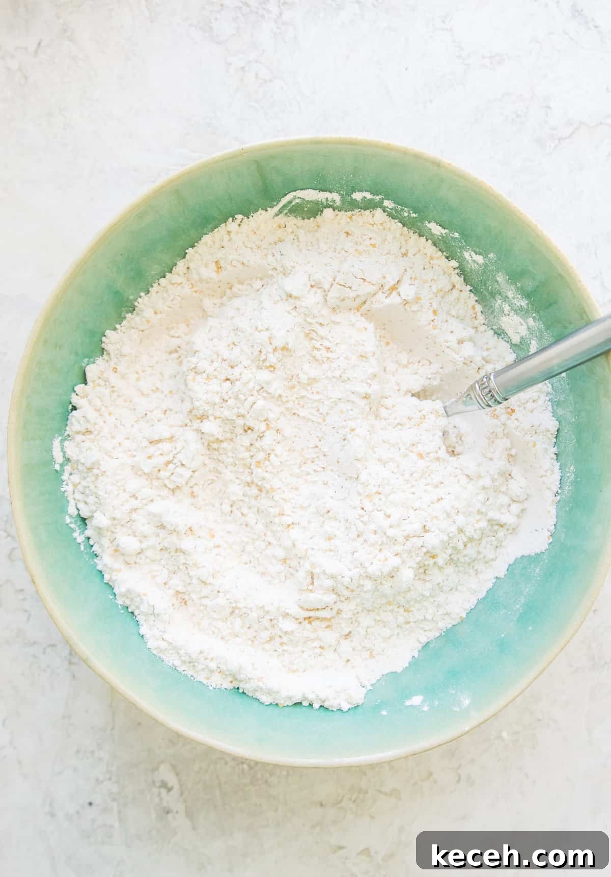 A bowl with flour and baking soda in it with a spoon in the mixture.