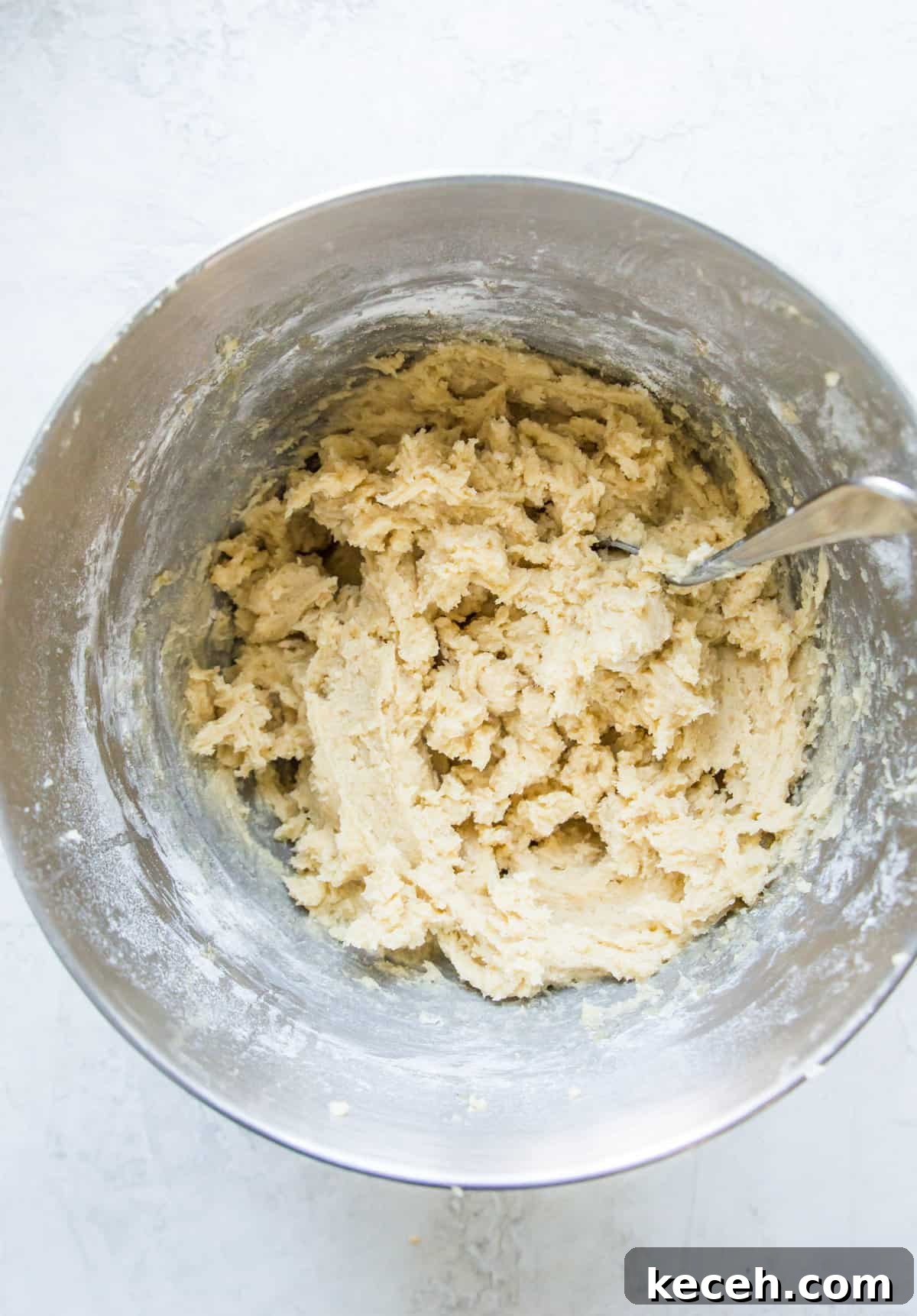 A bowl with cookie dough in it with a spoon in the dough.