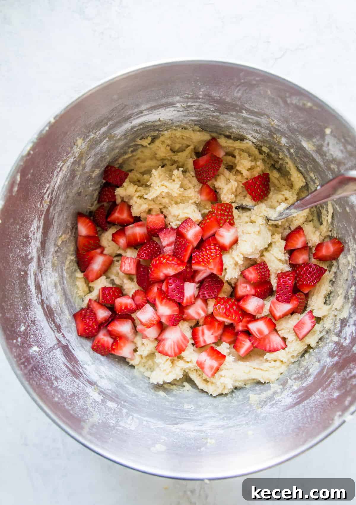 A bowl with cookie dough in it with chopped strawberries on top of the dough.