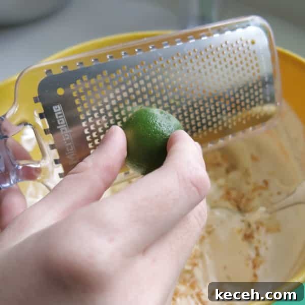A key lime being zested into a large bowl with the rest of the key lime ingredients.