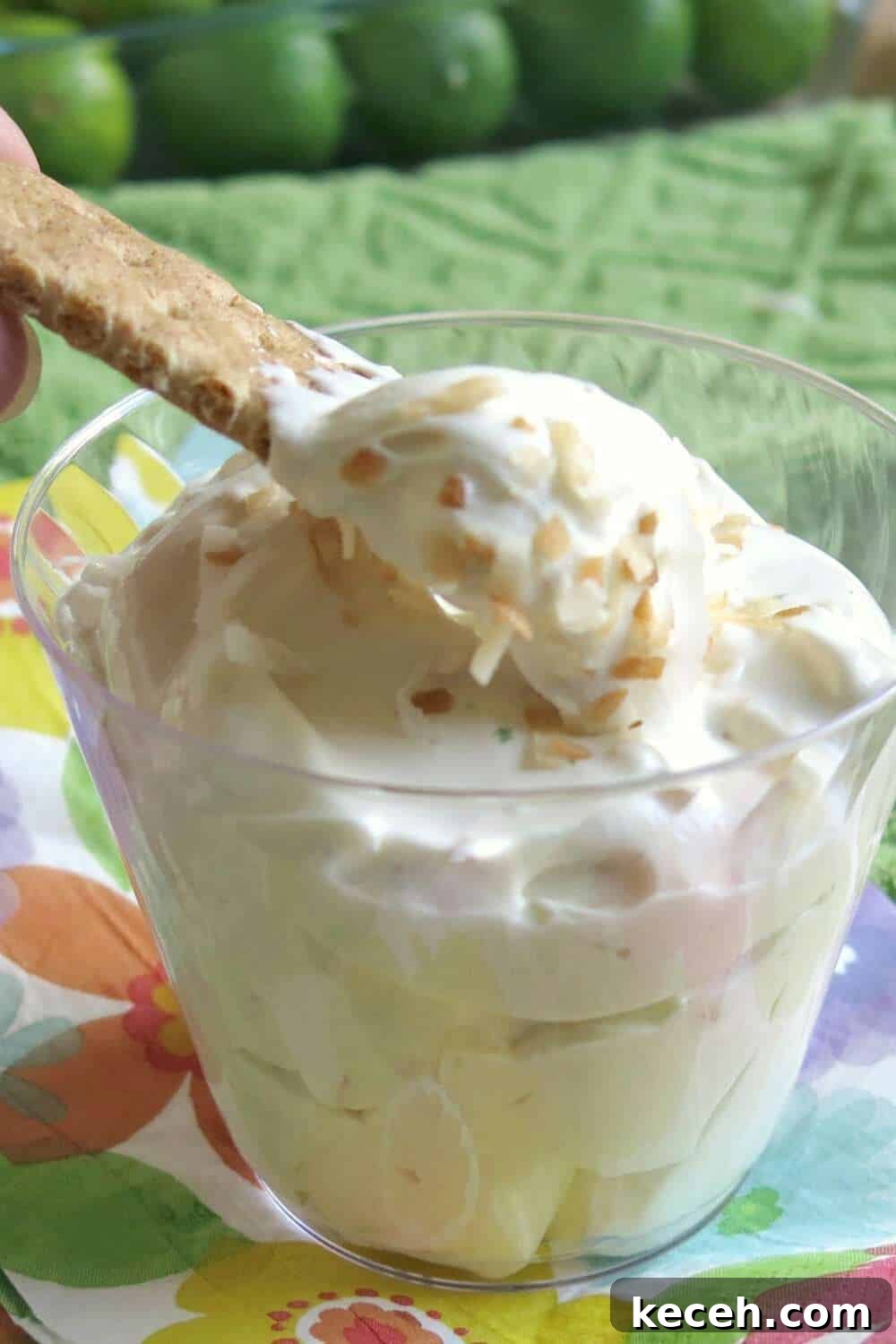 A graham cracker lifting out some Key Lime Pie Dip from a glass.