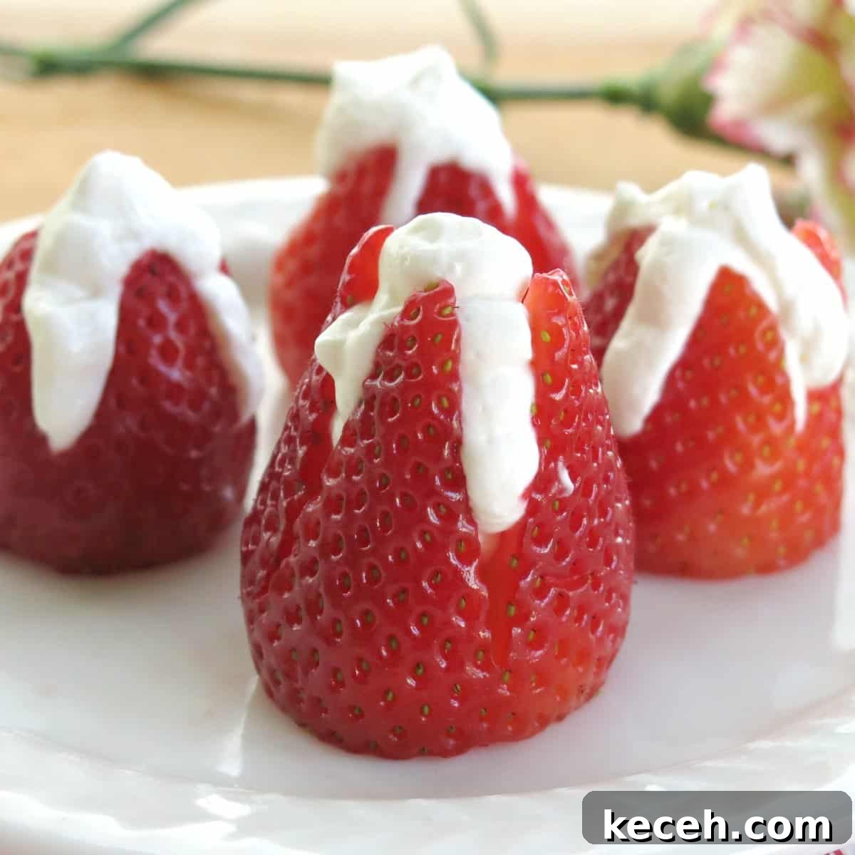 4 cheesecake stuffed strawberries on plate with flower behind it