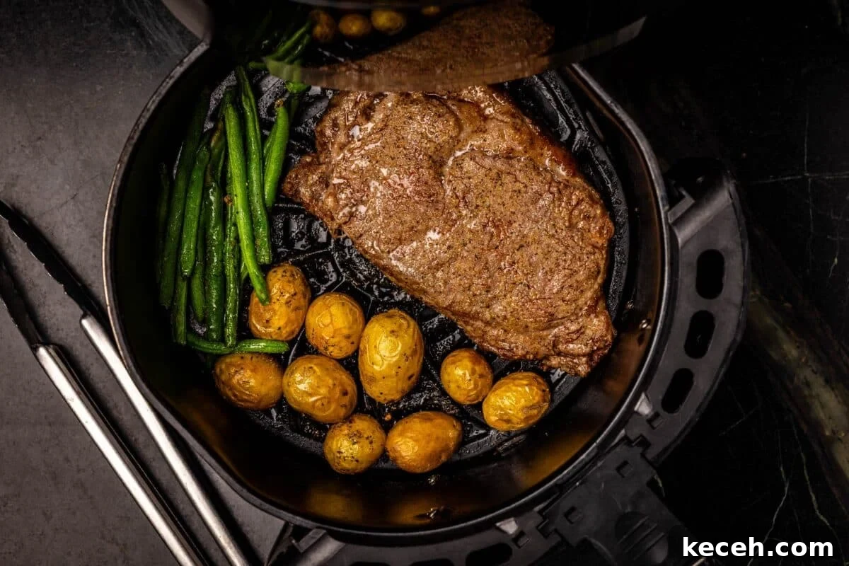 Crispy Air Fryer Steak with Roasted Potatoes & Green Beans 4 Steak, potatoes, and green beans in air fryer tray.