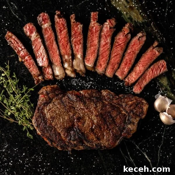 Crispy Air Fryer Steak with Roasted Potatoes & Green Beans 7 Sliced ribeye above whole ribeye next to garlic and thyme on black surface.