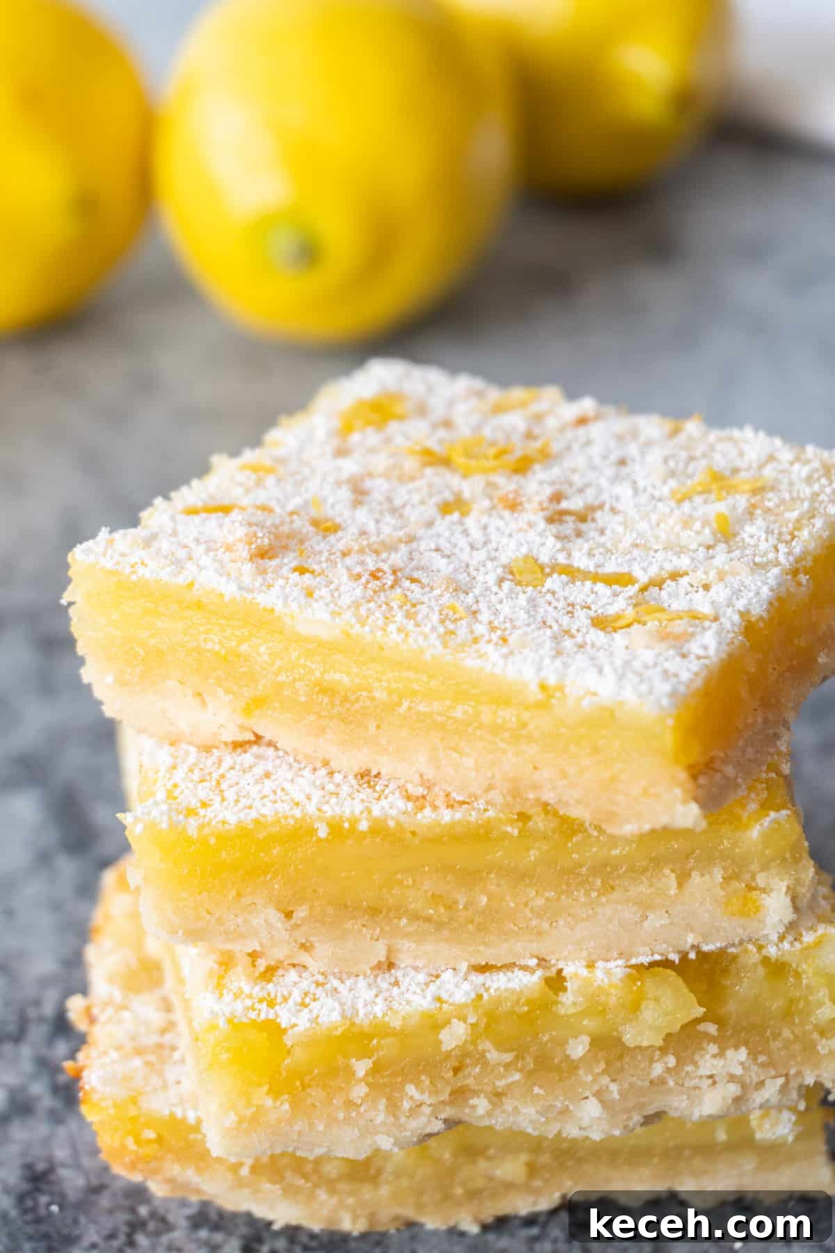 Classic Old-Fashioned Lemon Squares Recipe for Bright Dessert 4 Four lemon squares stacked on top of one another all sprinkled with powdered sugar and lemon zest.