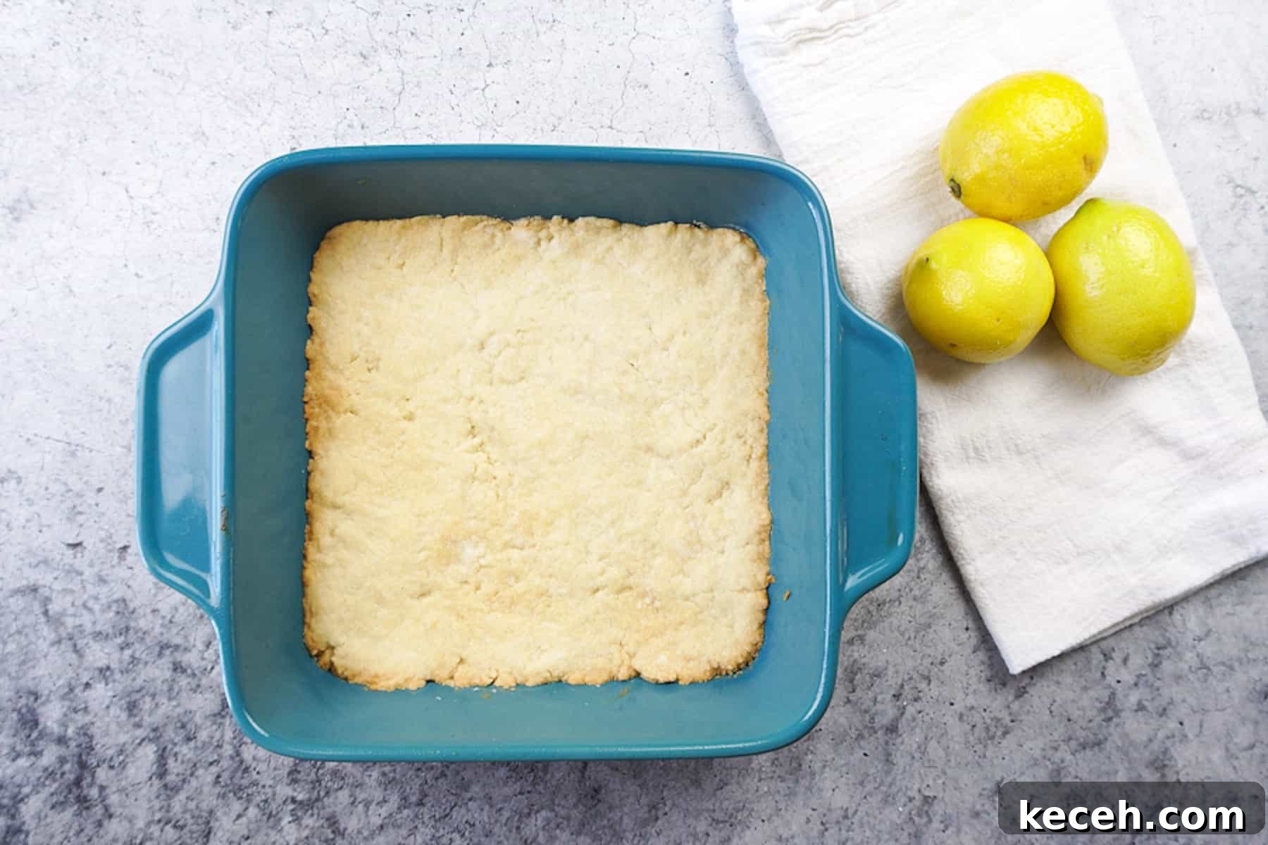 Classic Old-Fashioned Lemon Squares Recipe for Bright Dessert 7 lemon square crust baked in teal baking dish next to white towel and 3 lemons.