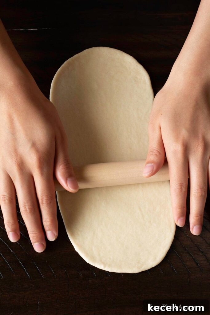 Rolling out the dough into an oblong oval with a rolling pin.