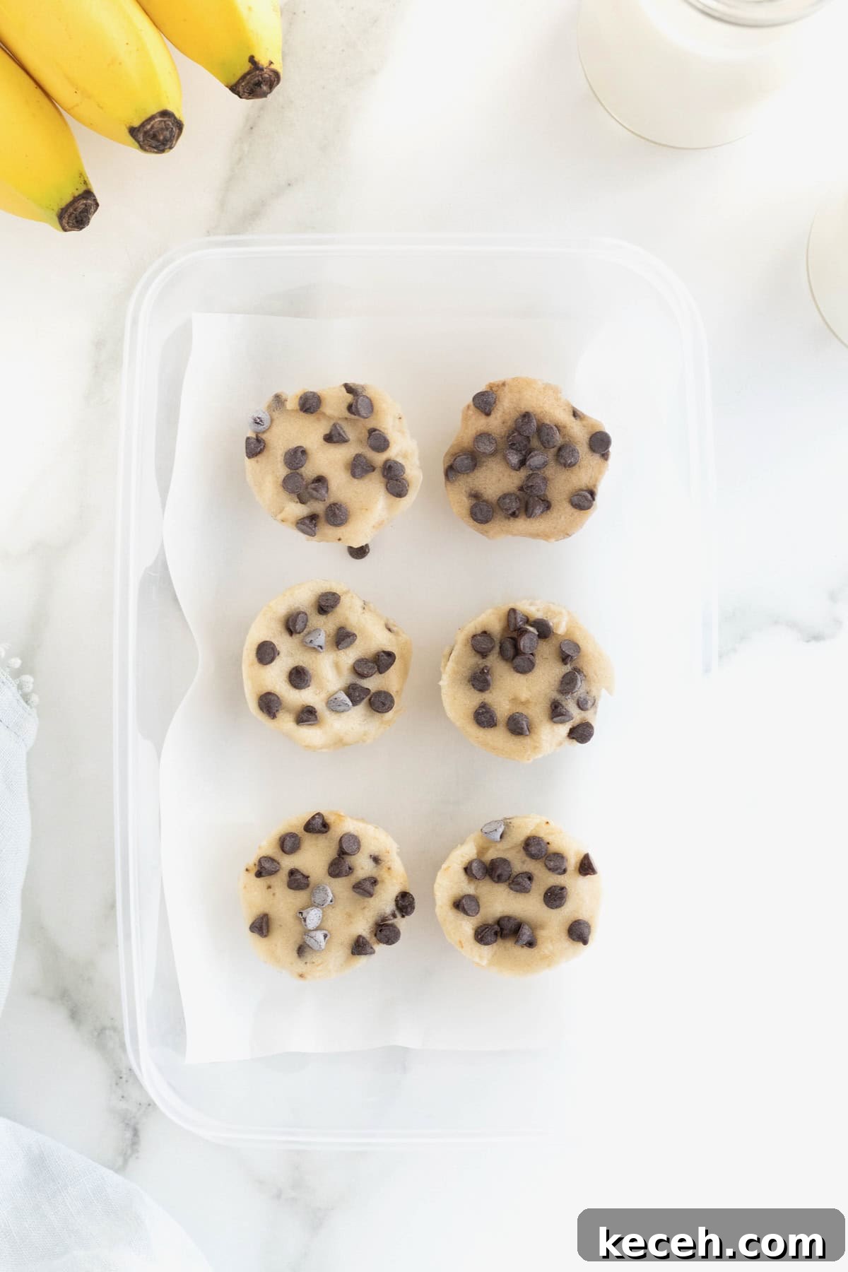 Banana Chocolate Chip Ice Cream Bites — 2-Ingredient Frozen Treats 11 Six banana ice cream bites with chocolate chips in a freezer-safe plastic container lined with parchment paper.