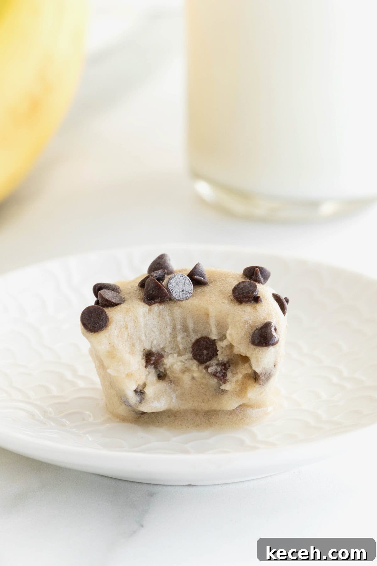 Banana Chocolate Chip Ice Cream Bites — 2-Ingredient Frozen Treats 3 A chocolate chip banana ice cream bite on a small white plate. The ice cream has a bite taken out of it.