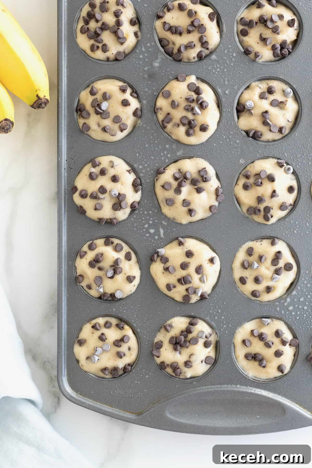 Banana Chocolate Chip Ice Cream Bites — 2-Ingredient Frozen Treats 4 Two-Ingredient Banana Chocolate Chip Ice Cream Bites in an aluminum mini muffin pan on a white marble counter.