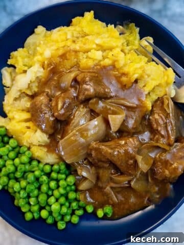 A blue dinner plate with peas and a helping of mashed potatoes smothered with braised steak and onions.
