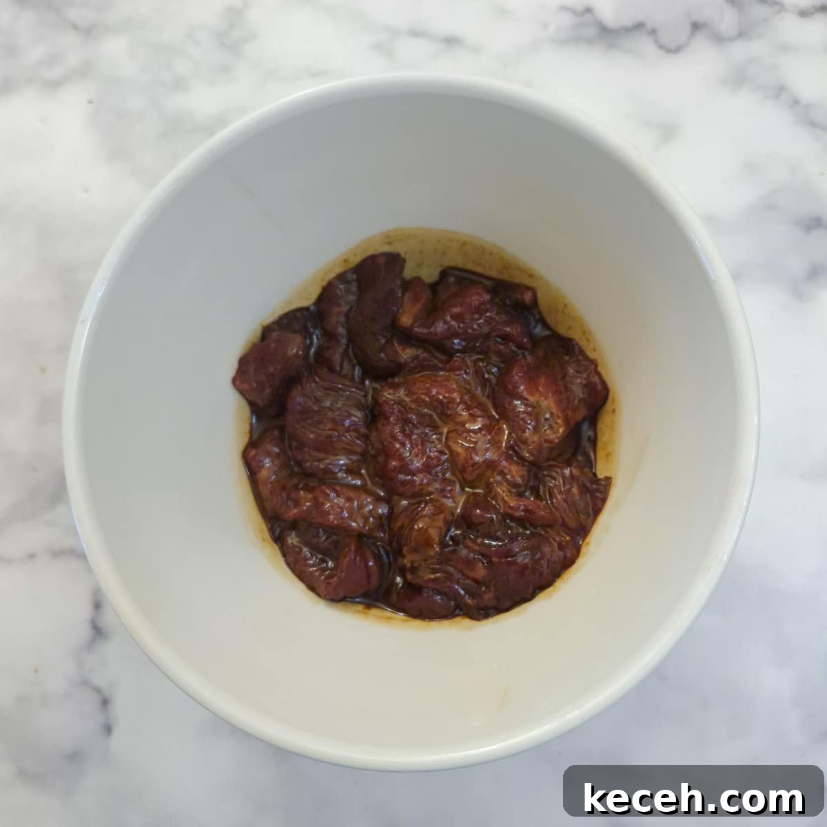 Steak strips marinating in a small white bowl in soy sauce and cornflour.