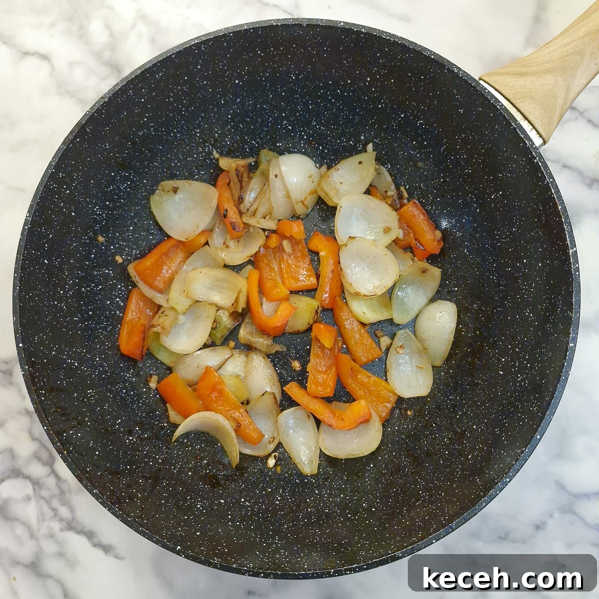 Onions and red peppers softening in a wok.