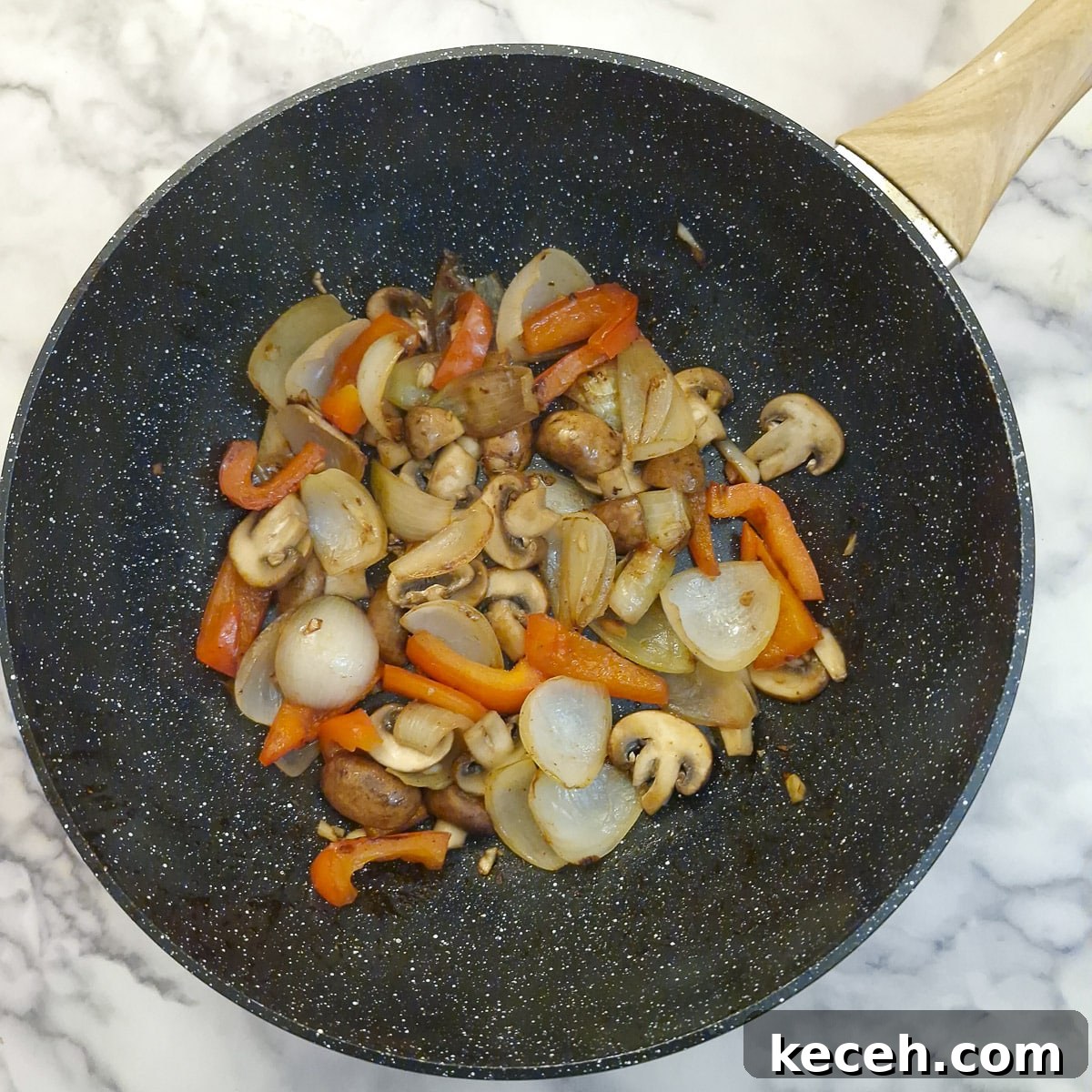 Mushrooms cooking with onions and red pepper in a wok.