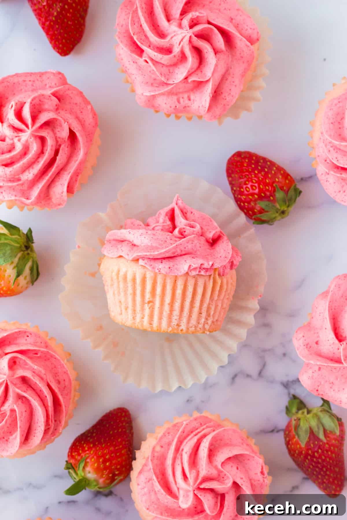 Strawberry-Filled Cupcakes with Fresh Strawberry Filling 2 Strawberry Filled Cupcakes with Strawberry Jello Buttercream on marble countertop with fresh strawberries around them.