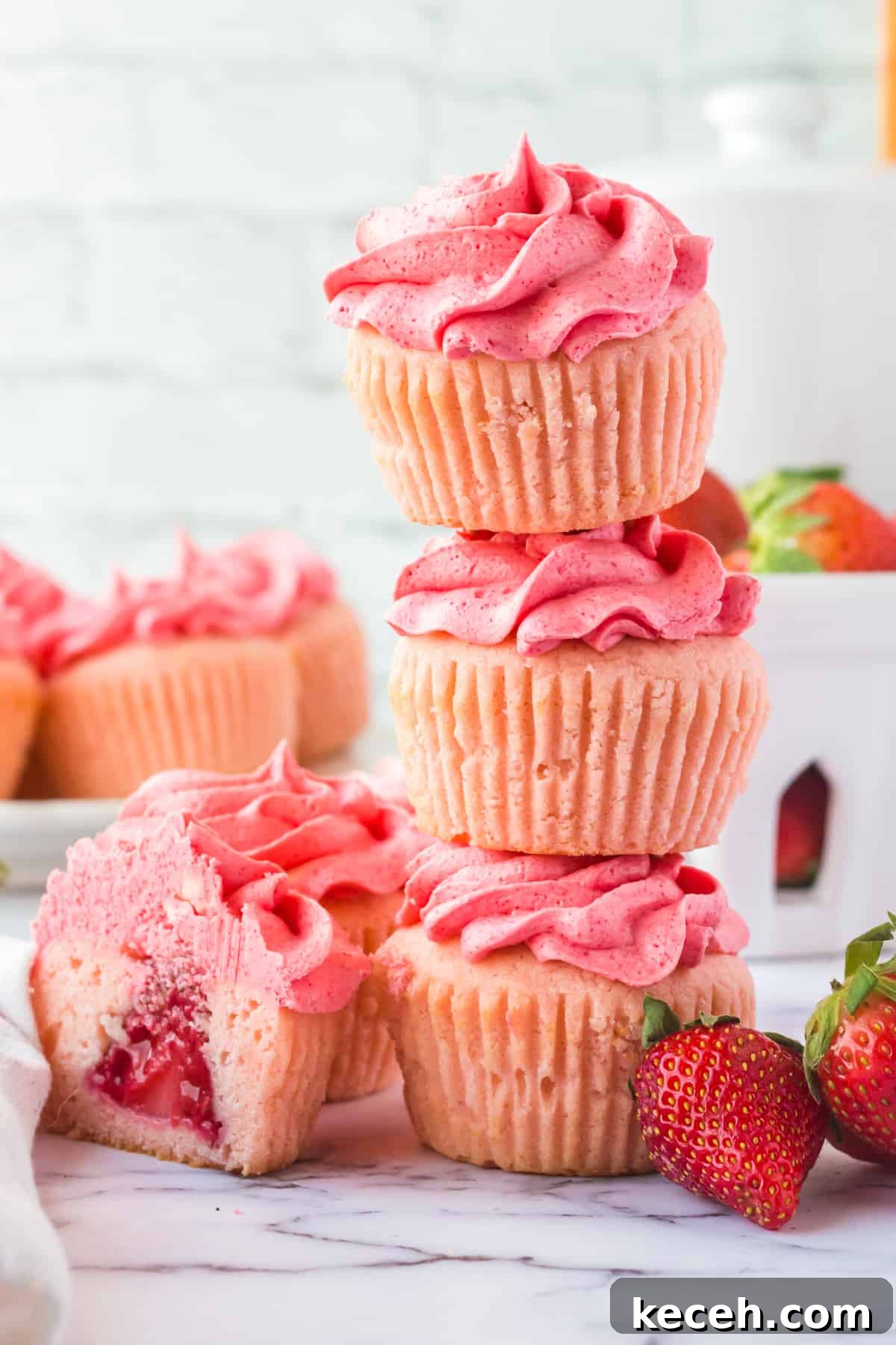 Strawberry-Filled Cupcakes with Fresh Strawberry Filling 10 3 strawberry cupcakes stacked on top of one another with another cupcake cut in half next to show strawberry in center