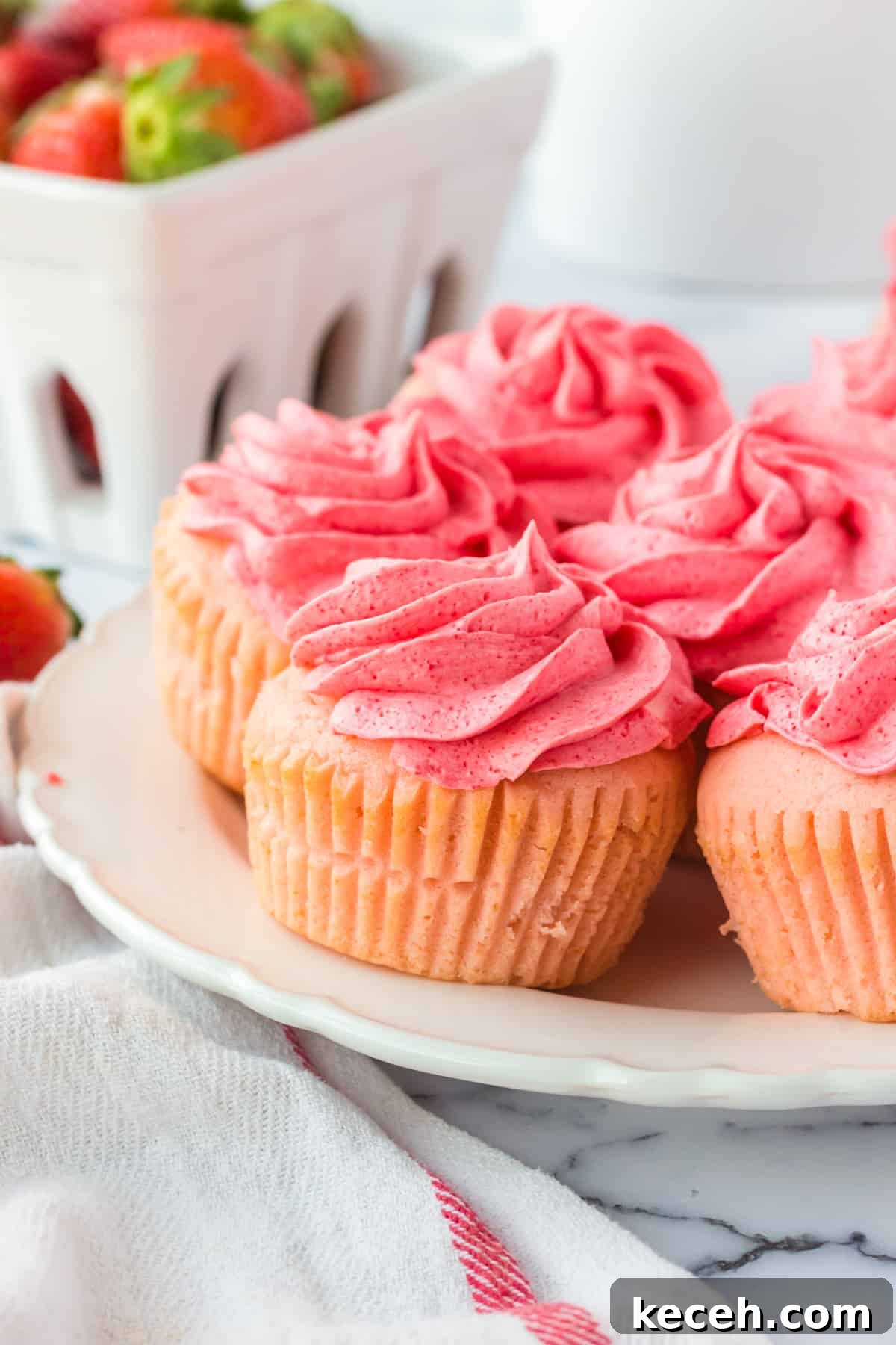 Strawberry-Filled Cupcakes with Fresh Strawberry Filling 11 Pink frosted cupcakes with fresh strawberries in the background