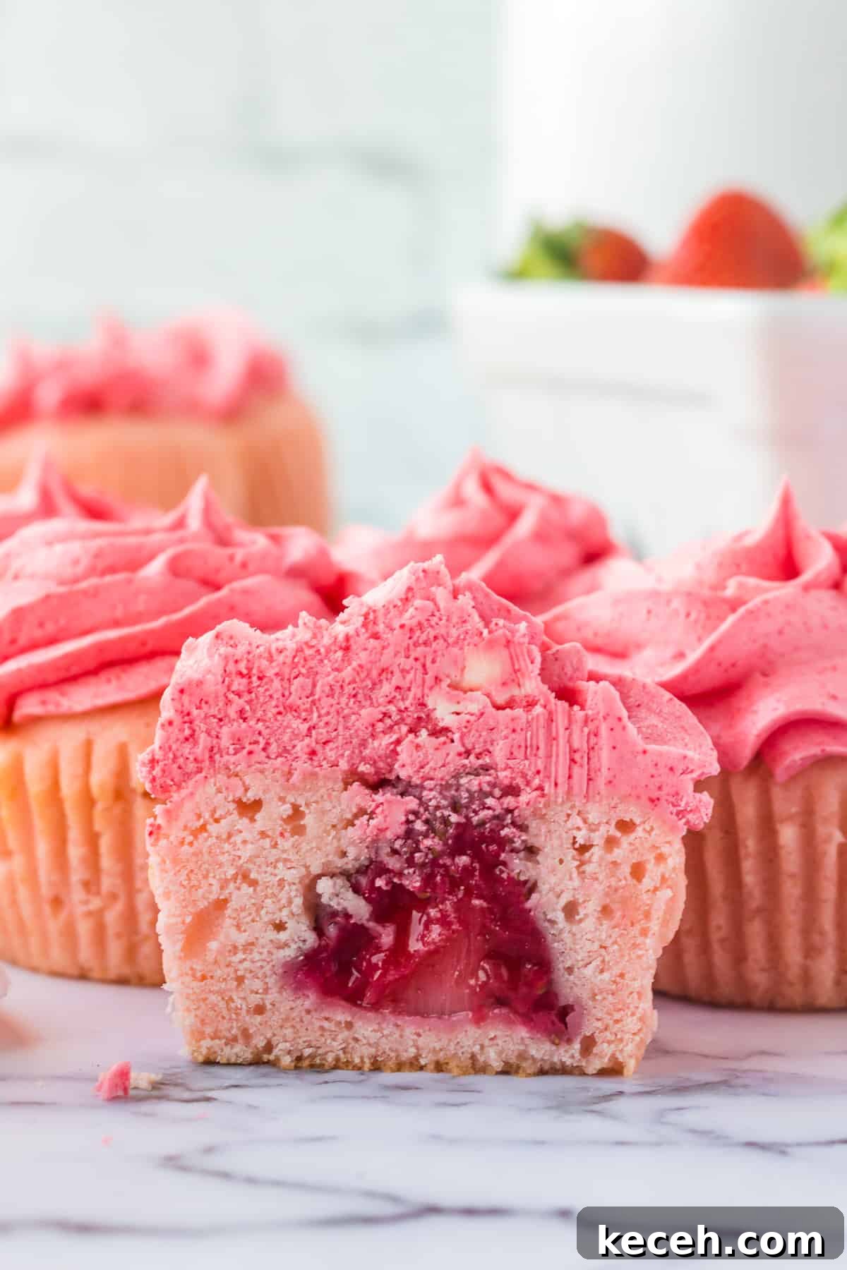 Strawberry-Filled Cupcakes with Fresh Strawberry Filling 3 Pink cupcake with pink frosting sliced in half to show whole strawberry in the center.