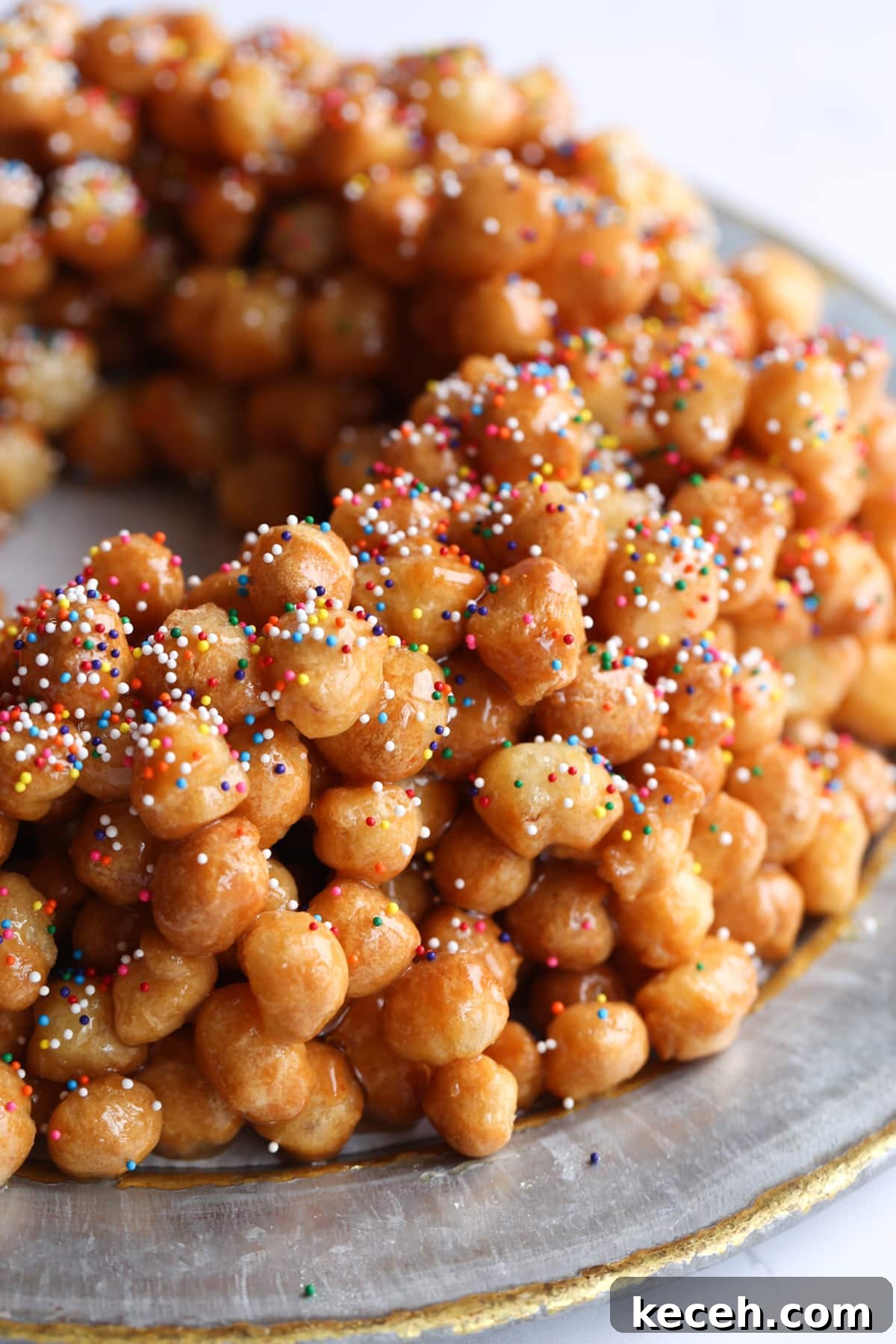 Authentic homemade Struffoli is such a fun Christmas dessert! Cute little balls of fried dough are coated in sweet honey and topped with your favorite holiday sprinkles. Rainbow sprinkles on top of Struffoli honey balls