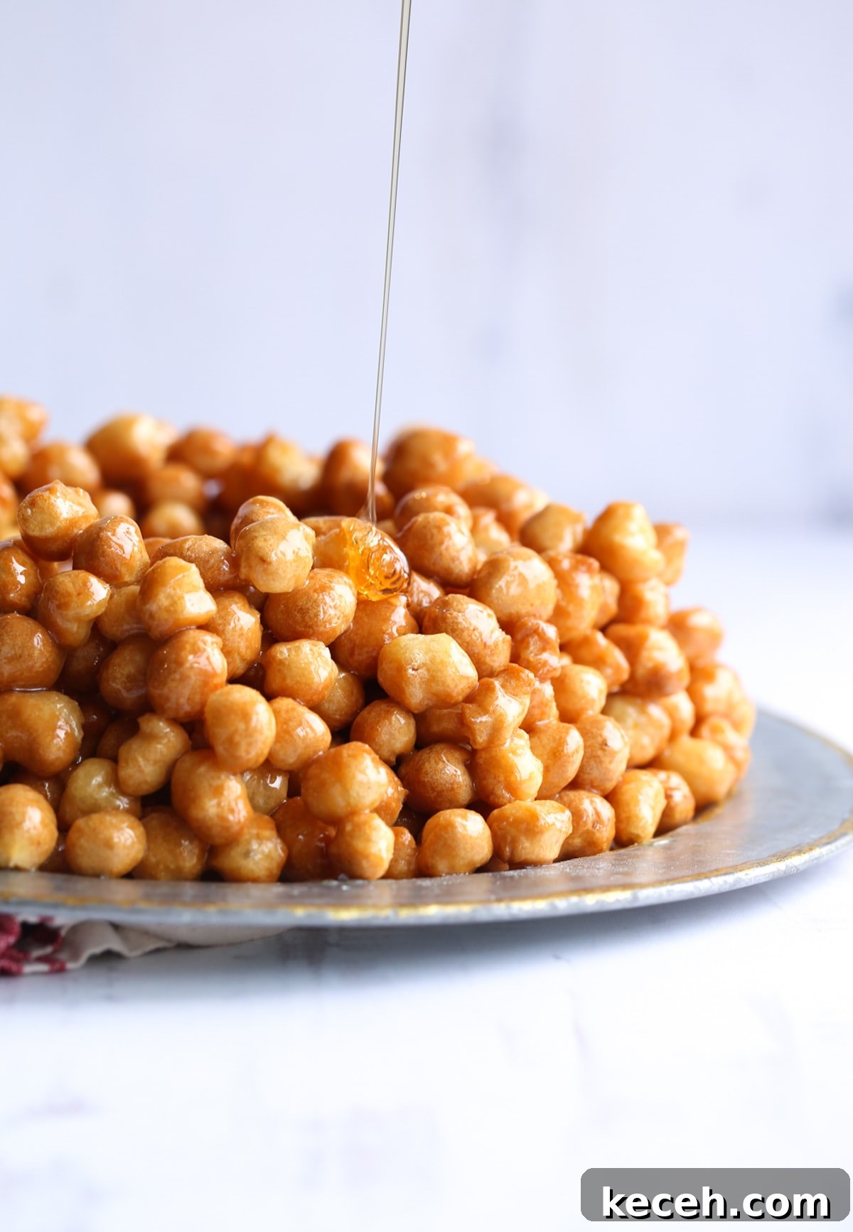Authentic homemade Struffoli is such a fun Christmas dessert! Cute little balls of fried dough are coated in sweet honey and topped with your favorite holiday sprinkles. Drizzling honey onto a pile of Struffoli on a platter