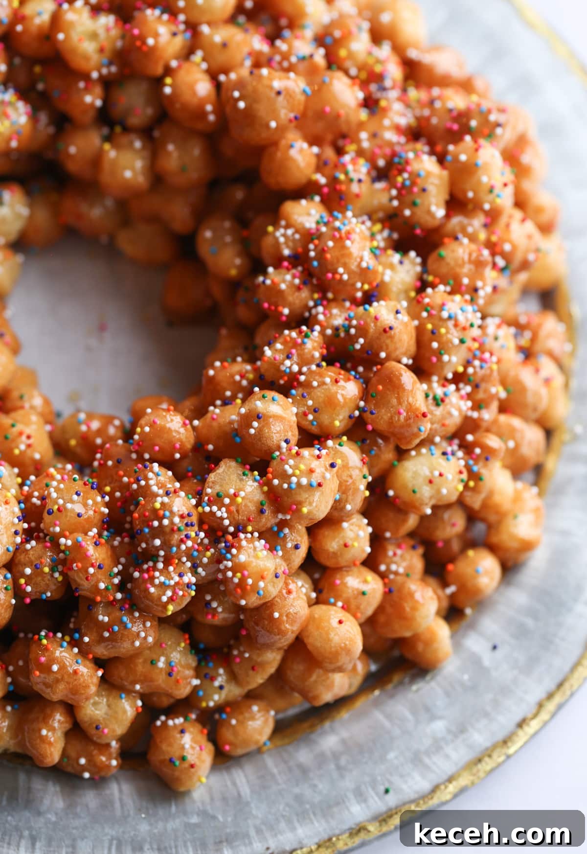 Authentic homemade Struffoli is such a fun Christmas dessert! Cute little balls of fried dough are coated in sweet honey and topped with your favorite holiday sprinkles. A pile of honey balls on a platter topped with nonpareil sprinkles