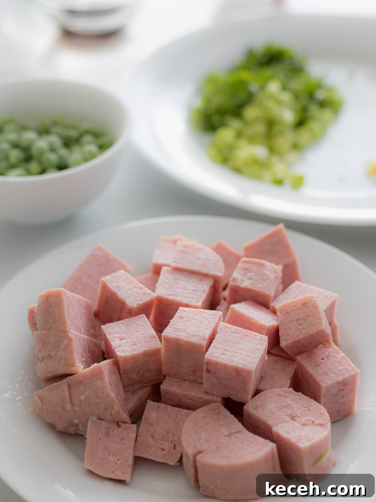 Simple Spam Fried Rice Recipe for Quick Weeknight Meals 7 spam cut into cubes on a white plate next to green peas in a bowl