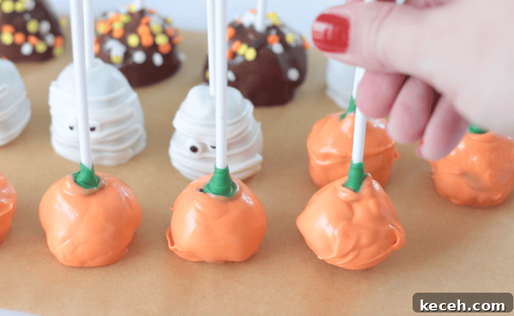 hand pressing lollipop stick into pumpkin brownie pop