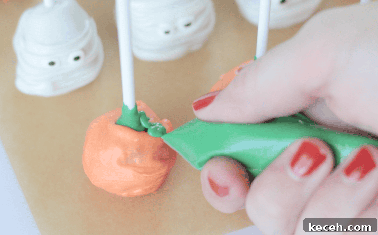 hand adding green candy melts to create pumpkin stem on lollipop