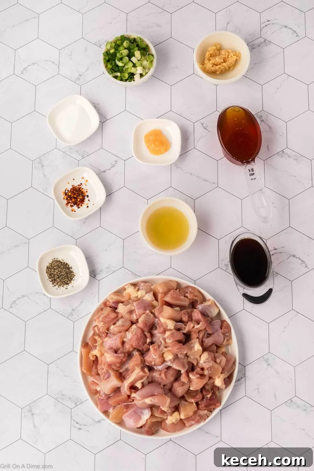 A plate of raw, chopped chicken—perfect for Blackstone Chicken—is surrounded by bowls of green onions, minced garlic, honey, soy sauce, and seasonings on a white hexagon-tiled surface, ready for a delicious Honey Garlic Chicken recipe.