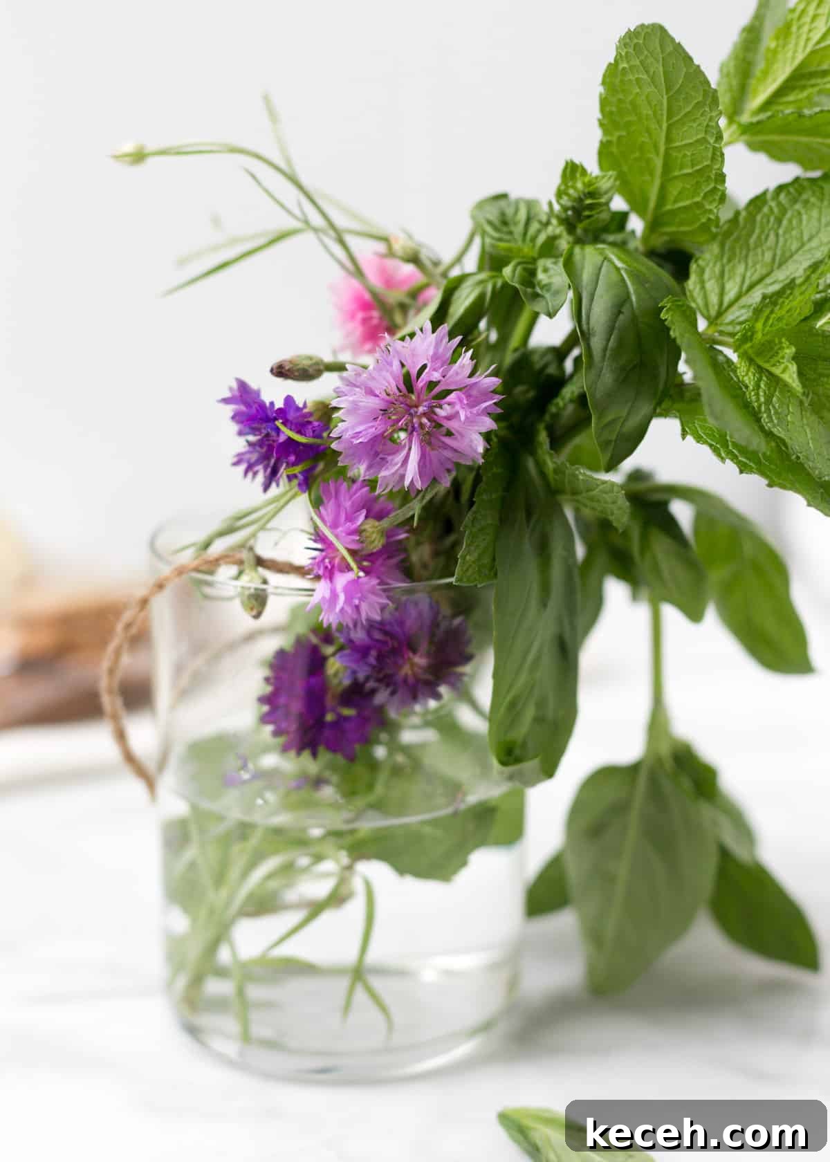 Citrus Salad with Honey-Balsamic Vinaigrette Recipe 3 glass jar filled with fresh basil, mint, and pink and purple edible flowers on a white marble board