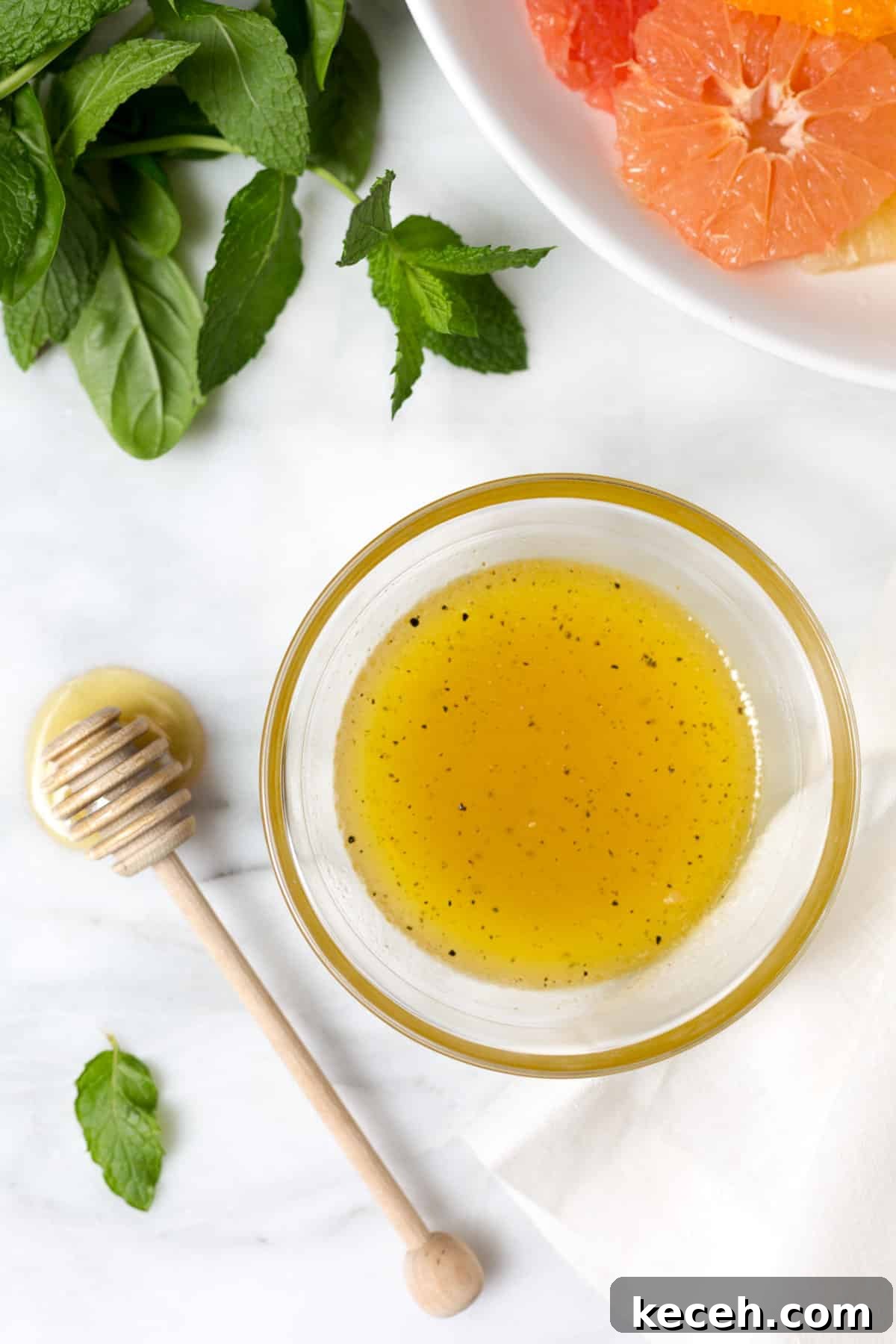 Citrus Salad with Honey-Balsamic Vinaigrette Recipe 5 overhead photo of honey balsamic vinaigrette in a glass bowl next to a honey dipper on a white marble board