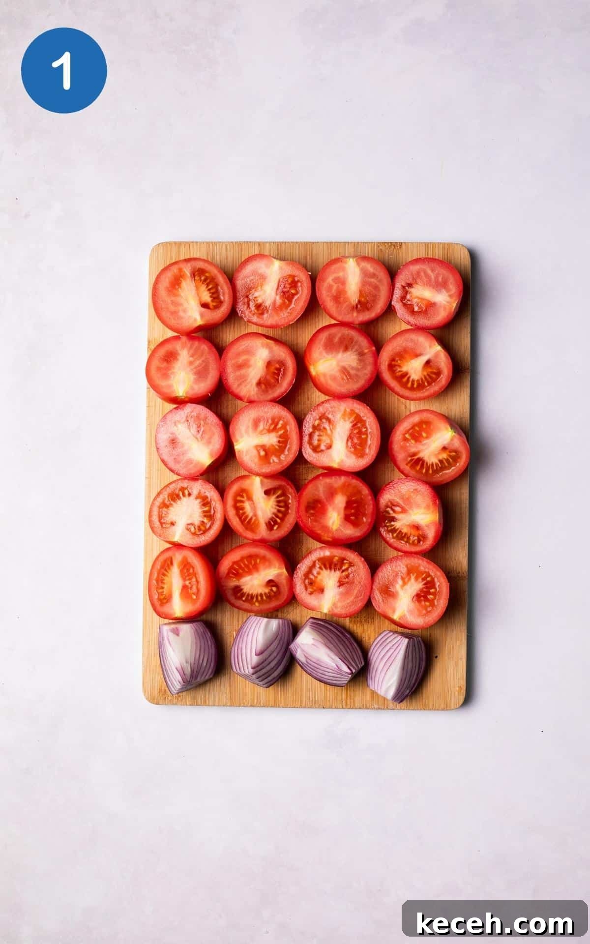 Creamy Roasted Tomato Soup Recipe with Garlic and Basil 4 Tomatoes sliced in half and onions sliced in quarters lined up on a wooden chopping board.