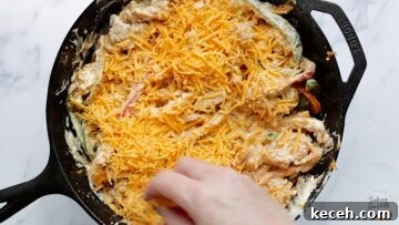 Topping the chicken fajita casserole with shredded cheddar cheese before baking.