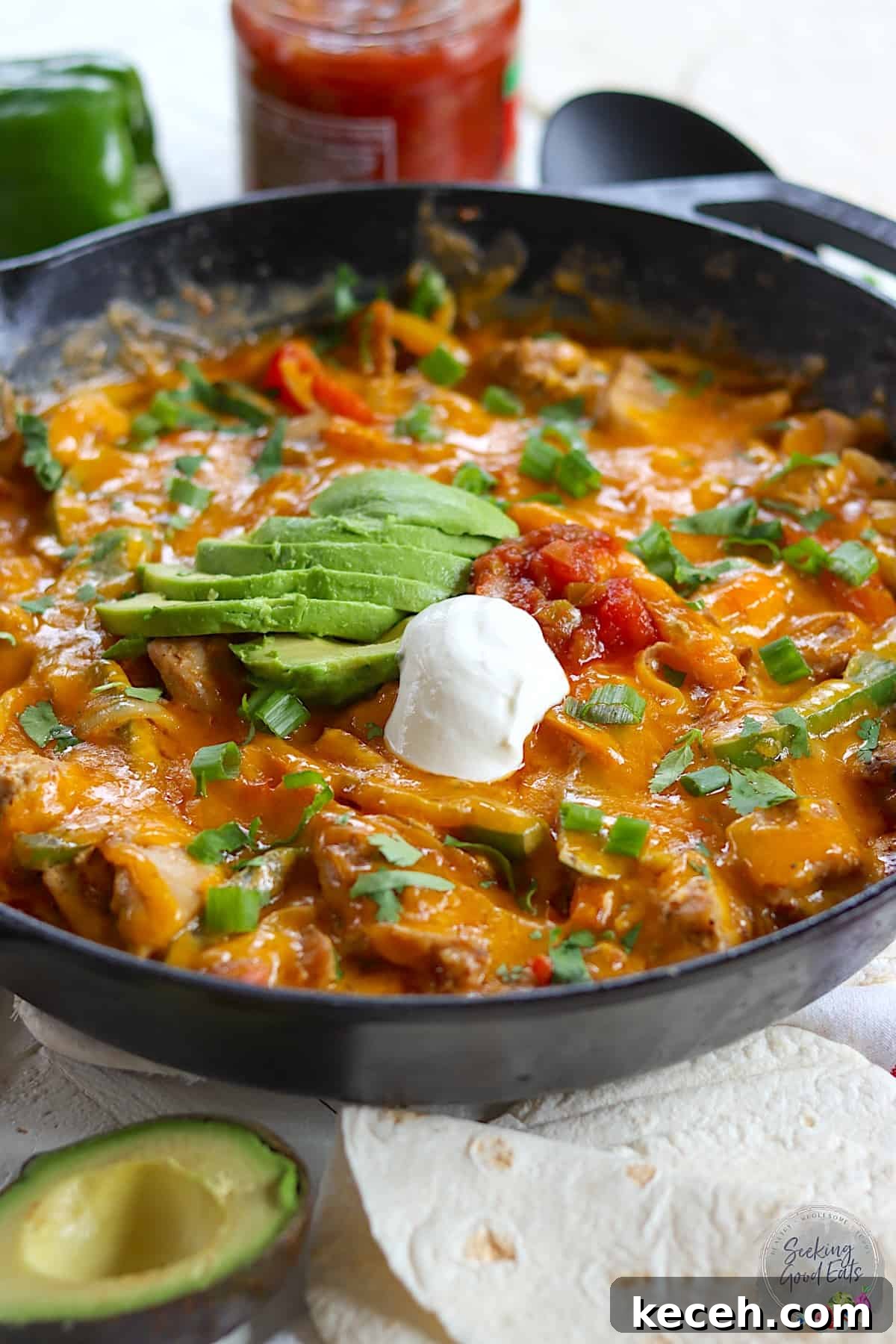 Chicken fajita casserole in a cast iron skillet with sour cream and avocado slices.