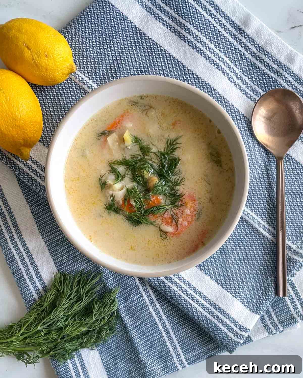 Authentic Greek Chickpea Soup (Revithosoupa) Recipe 2 A bowl of Greek Chickpea Soup garnished with dill sits on a blue and white linen with a spoon, fresh dill, and lemons.