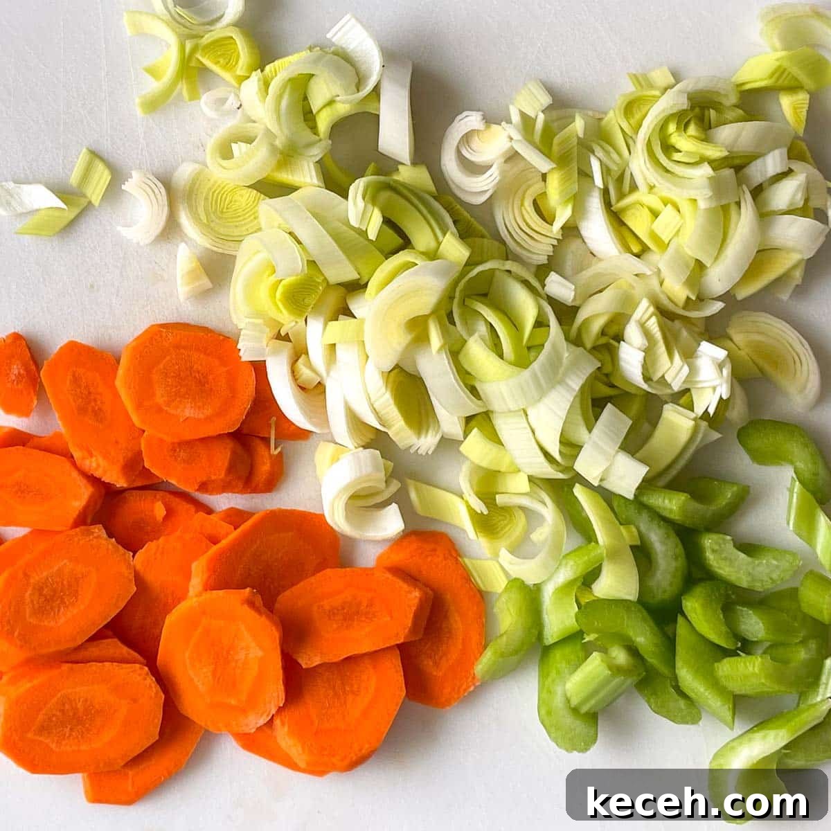 Authentic Greek Chickpea Soup (Revithosoupa) Recipe 5 Carrot, celery, and leek sliced on a bias are shown on a white cutting board.