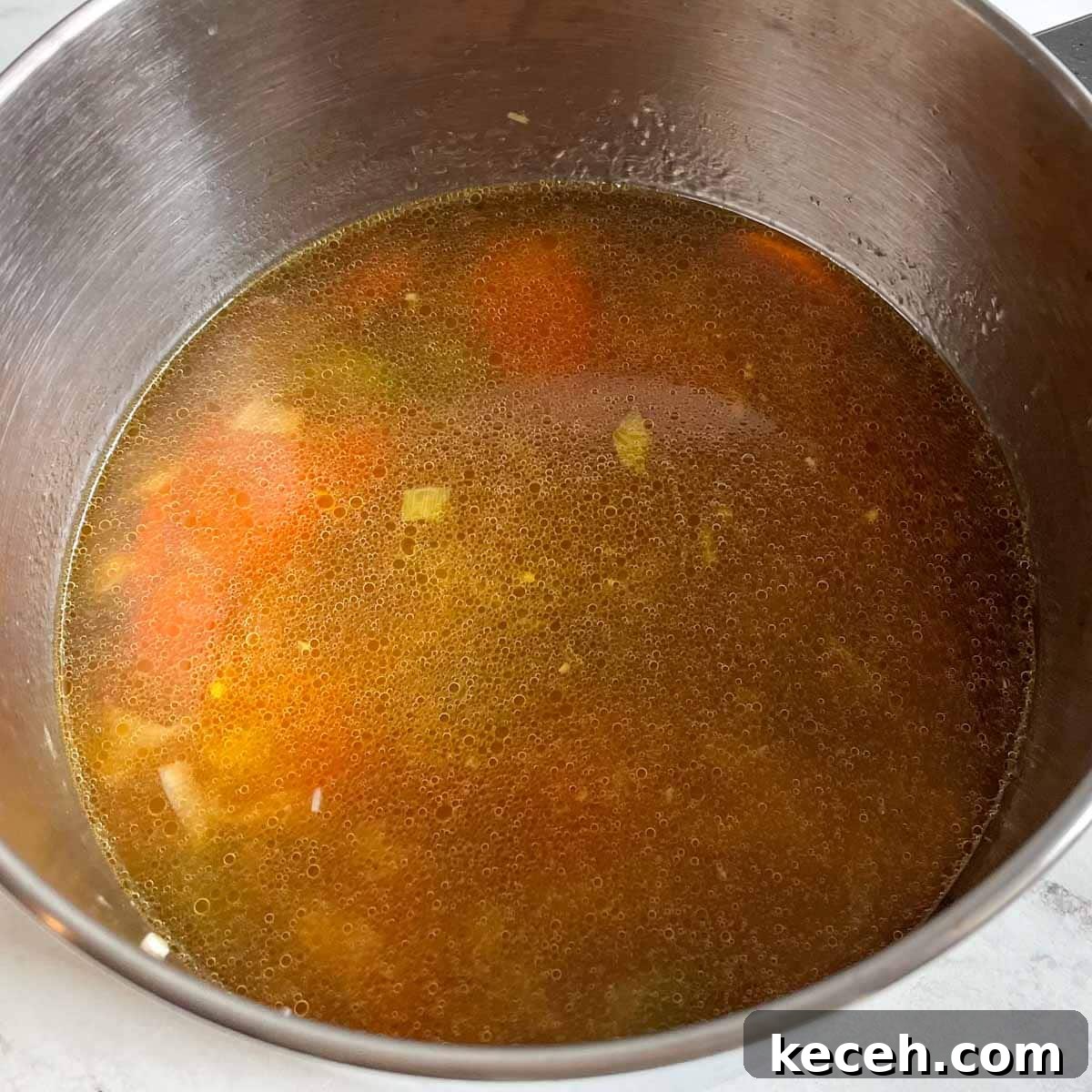 Authentic Greek Chickpea Soup (Revithosoupa) Recipe 9 Vegetable broth with sliced carrots, celery, and leek are shown in a stainless steel pot.