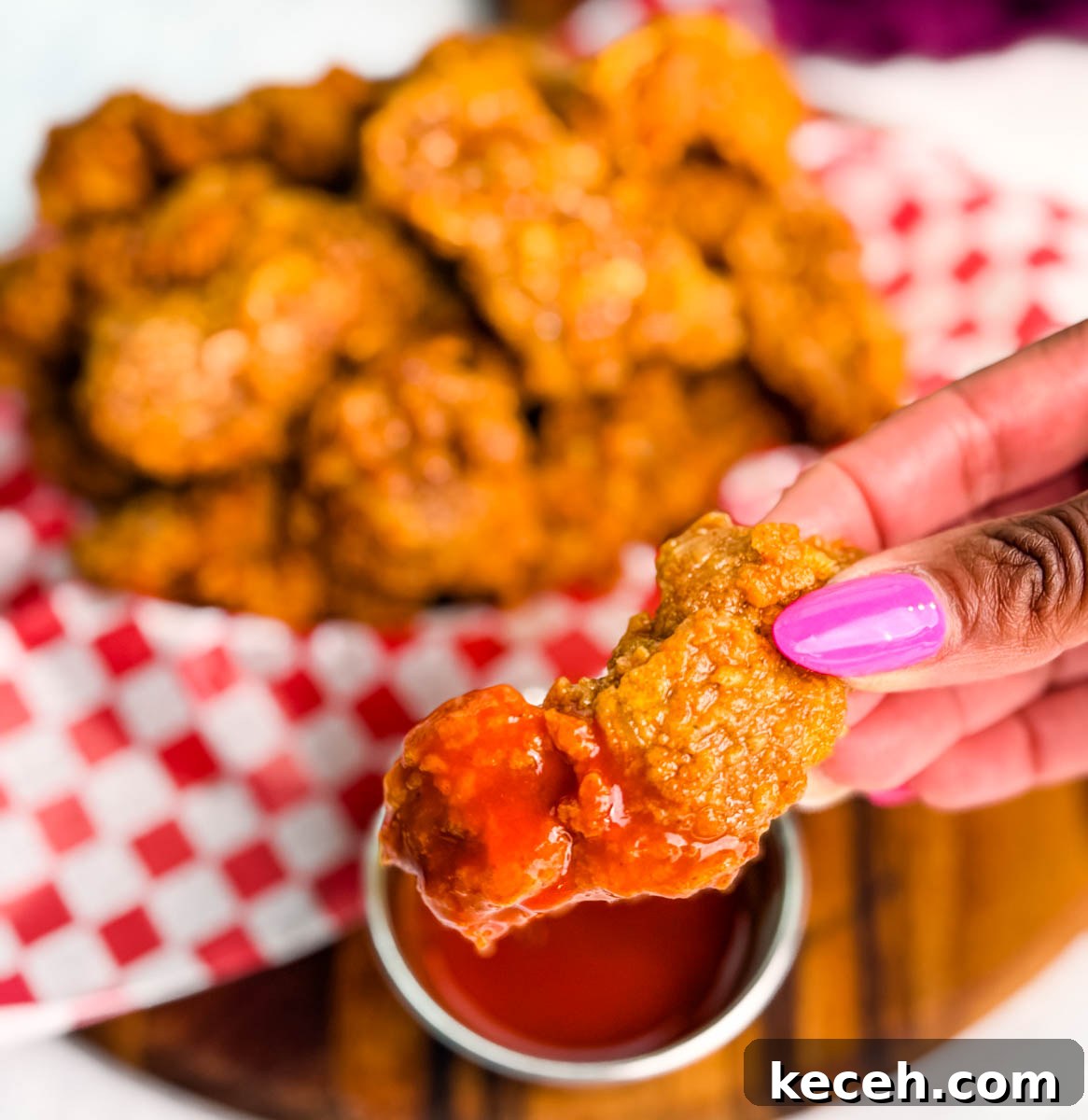 Crispy Fried Chicken Gizzards Recipe: Southern-Style Crunch 12 Close-up of a hand holding a crispy fried chicken gizzard dipped in bright red hot sauce, with a basket of fried gizzards blurred in the background.